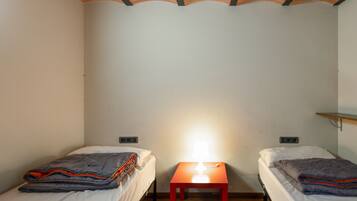 Una habitación pequeña con dos camas, una mesita de noche y un estante.