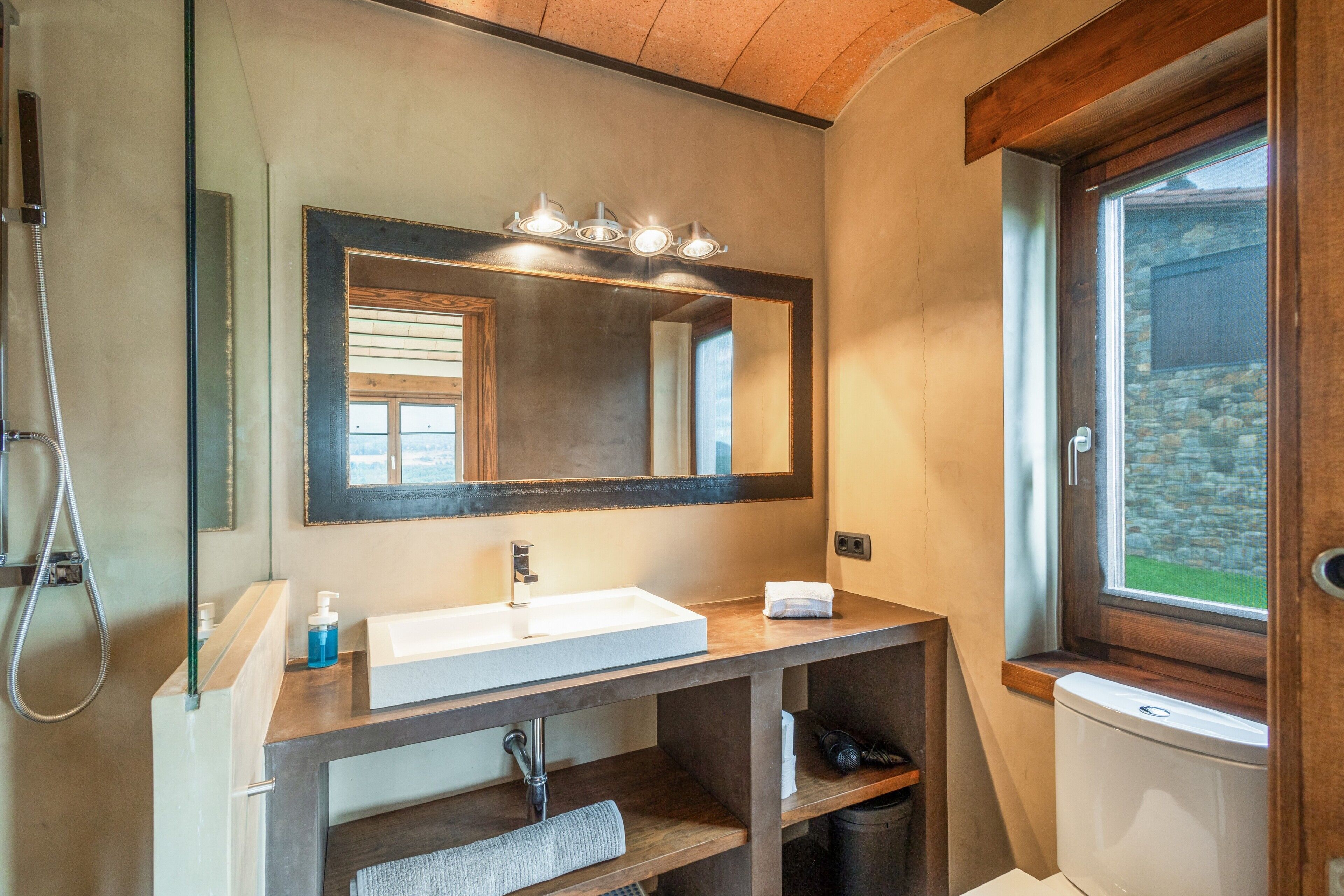 Un baño con un espejo grande, un lavamanos, una ducha y una ventana.