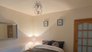 Une chambre à coucher avec un lit, une table de chevet, une lampe, un miroir et une porte en bois.