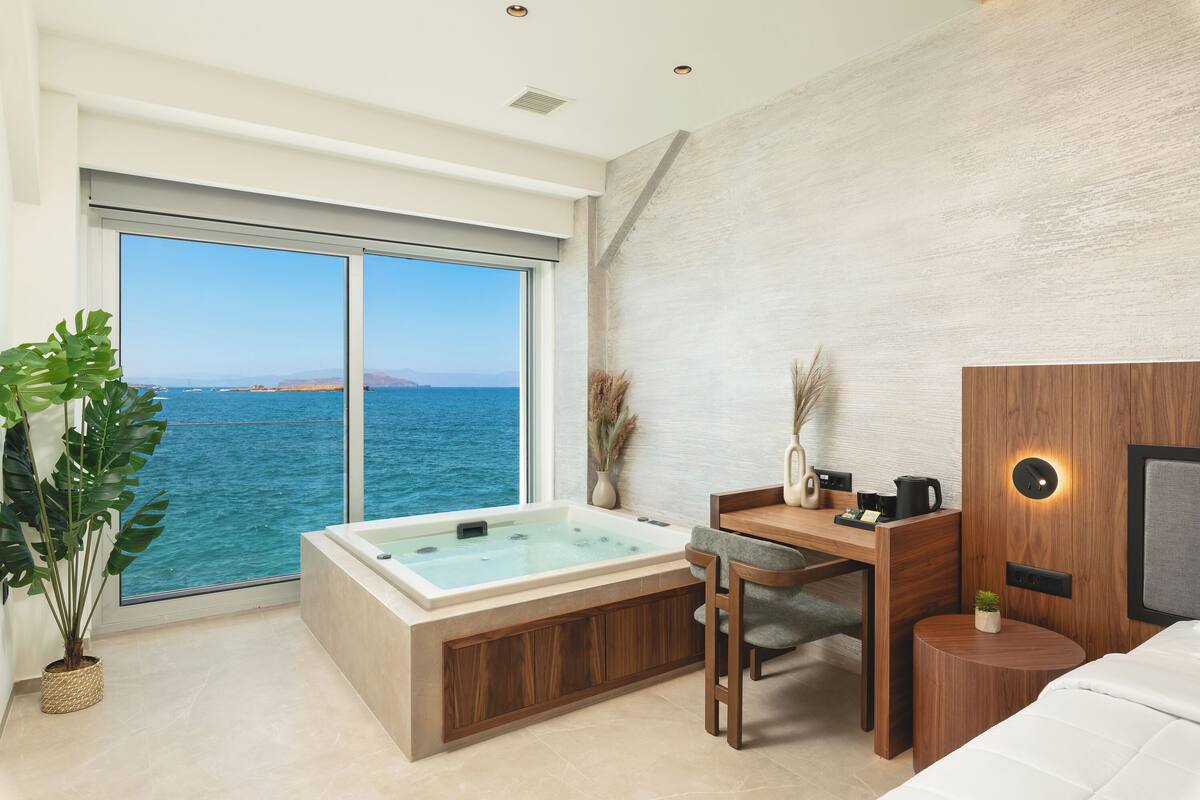 A modern room with a large window, a bathtub, a desk, and a small round table.