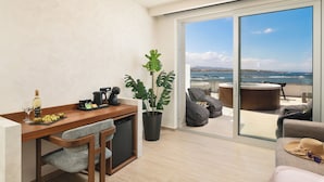 A modern living room with a wooden desk, a potted plant, and a view of the sea through large sliding doors. - Elia Sea Suites (Chania)