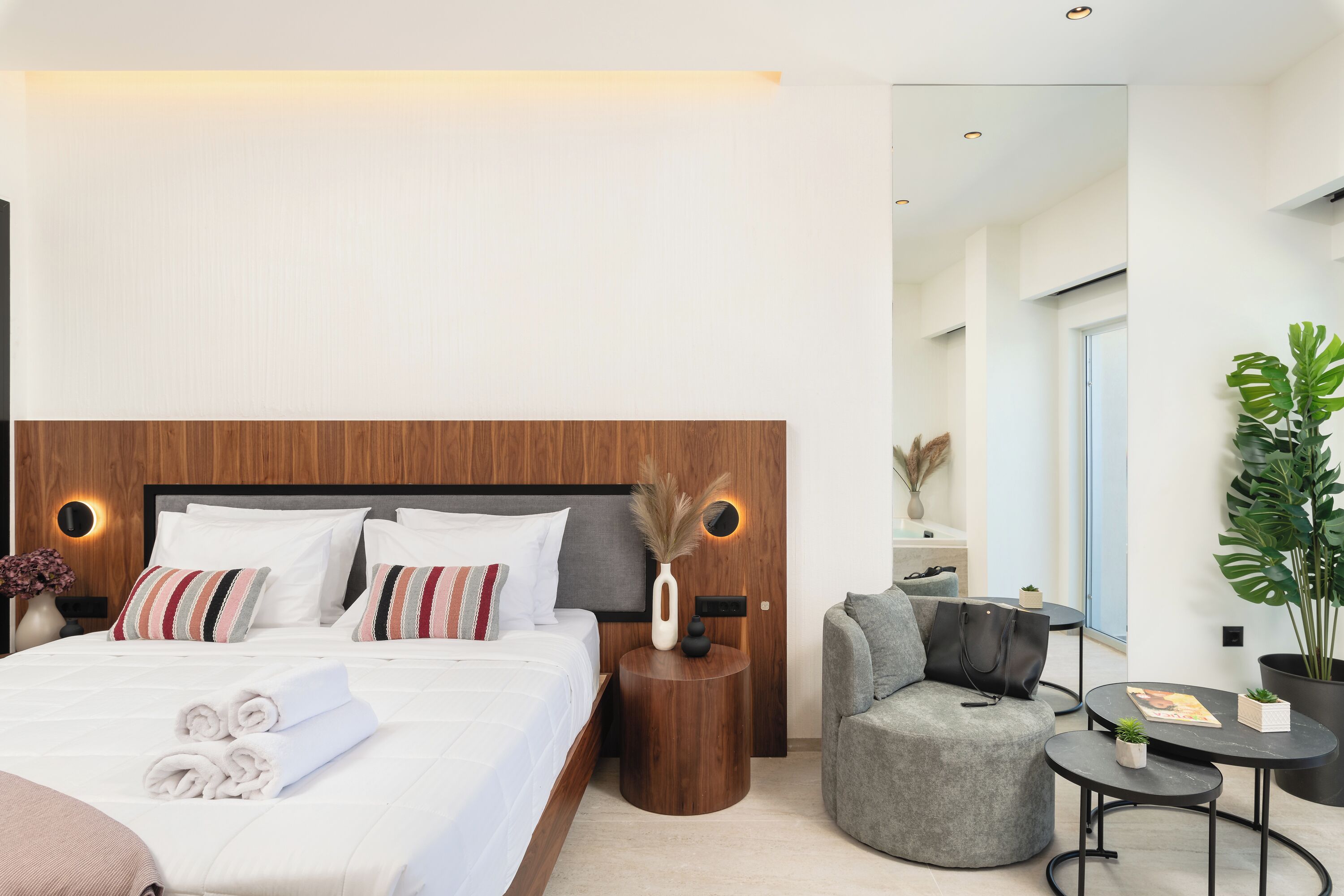 A modern hotel room with a large bed, bedside tables, a seating area with a sofa and chairs, and a potted plant.
