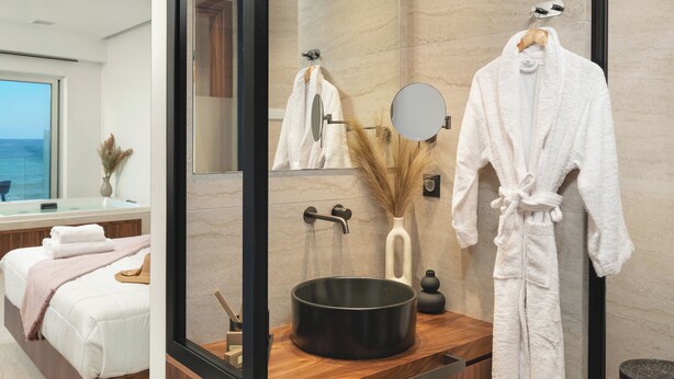 A modern bathroom with a large mirror, a black sink, and a robe hanging on the wall. - Elia Sea Suites (Chania)