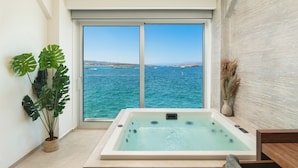 A room with a large window, a jacuzzi, and a view of the sea. - Elia Sea Suites (Chania)