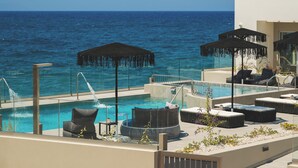 A rooftop pool area with lounge chairs, umbrellas, and a view of the ocean. - Elia Sea Suites (Chania)