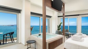 A modern room with a large bathtub, a bed, a TV, and a view of the sea. - Elia Sea Suites (Chania)