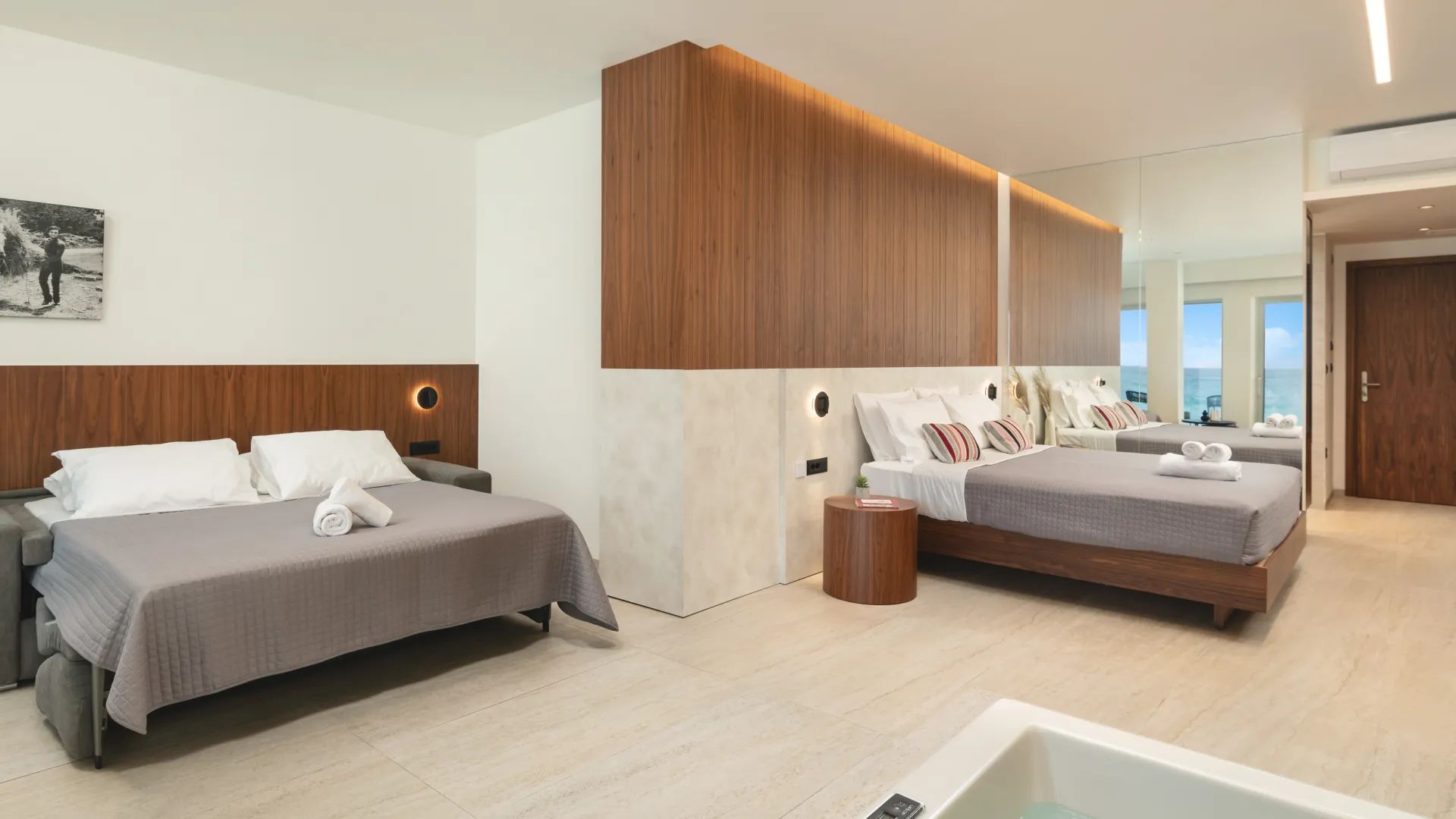 Ein modernes Hotelzimmer mit zwei Betten, einem großen Spiegel und Blick auf das Meer.