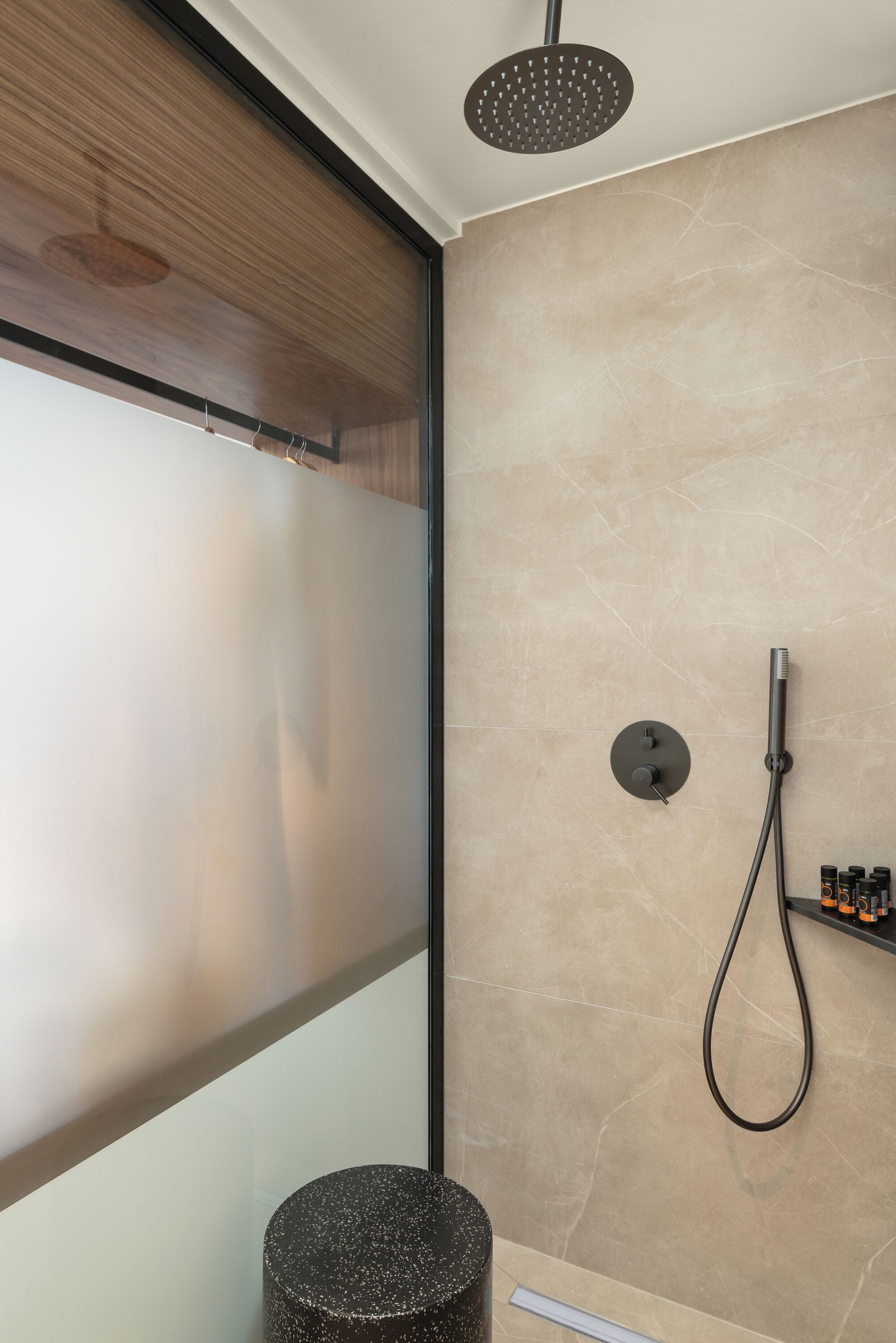 Un baño moderno con ducha, un lavabo redondo y un taburete pequeño.