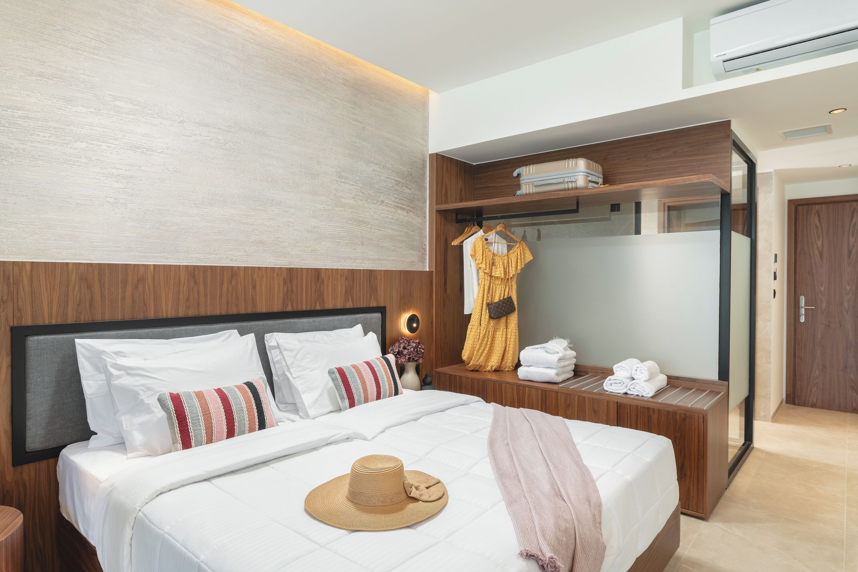 A modern hotel room with a large bed, a wardrobe, a vanity with a mirror, and a hanging robe.