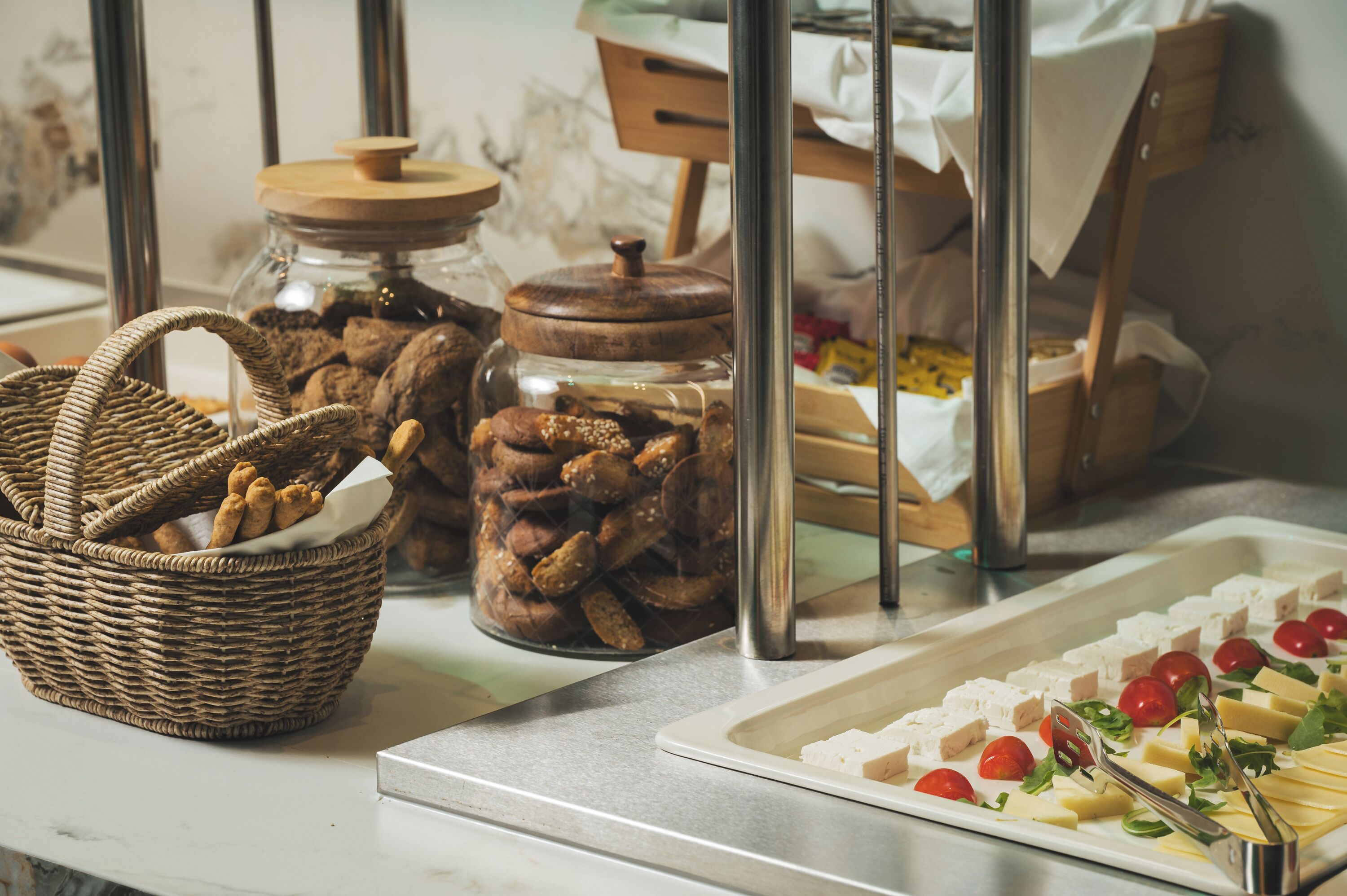 Une table de buffet proposant divers aliments, notamment un panier en osier, des bocaux de noix et un plateau de fromage et de tomates.