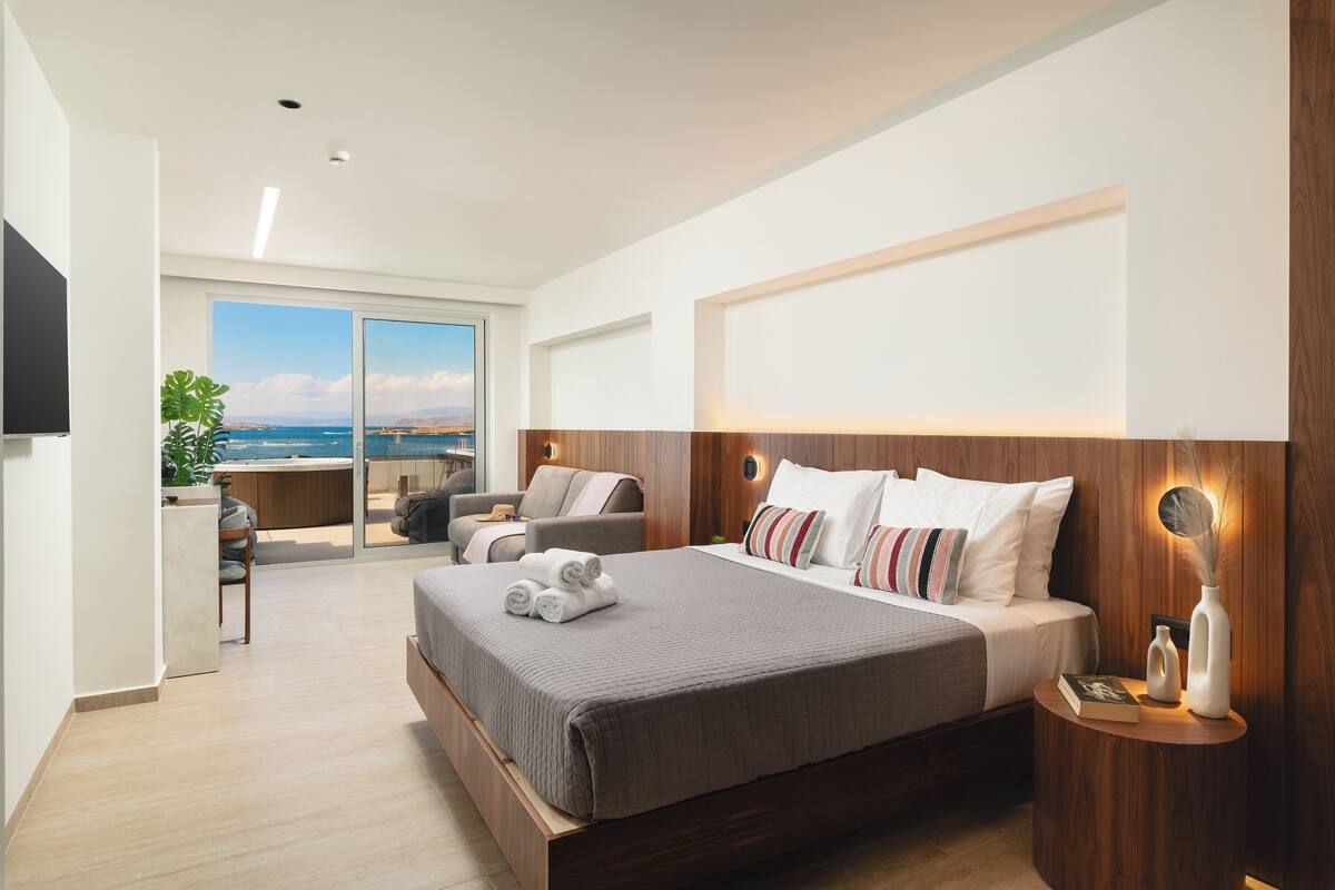 A modern hotel room with a large bed, a seating area with a view, and a wooden accent wall.