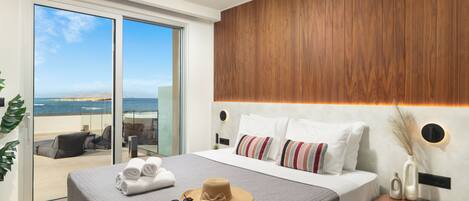 Una habitación de hotel moderna con una cama grande, vista al mar a través de una puerta corredera y un panel decorativo de madera.