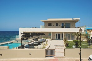 Un hotel moderno con piscina, asientos al aire libre y vistas al océano.