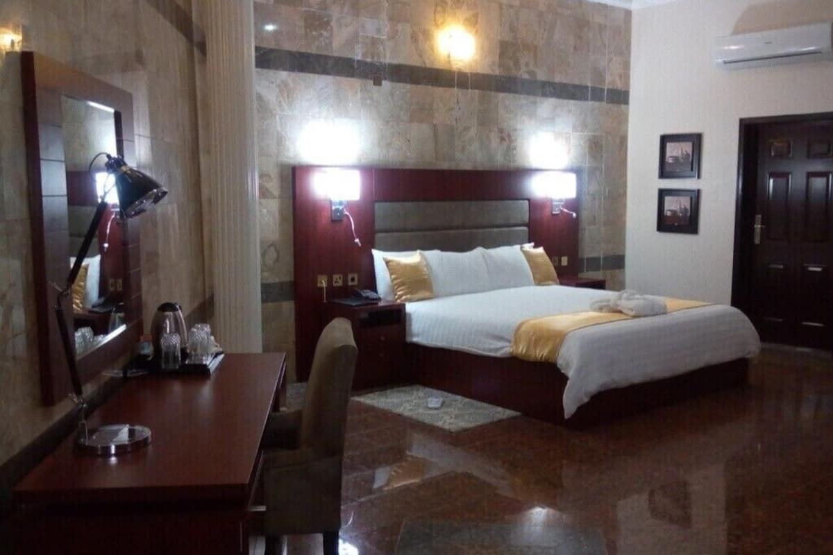 A hotel room with a large bed, a desk with a lamp, and a mirror.