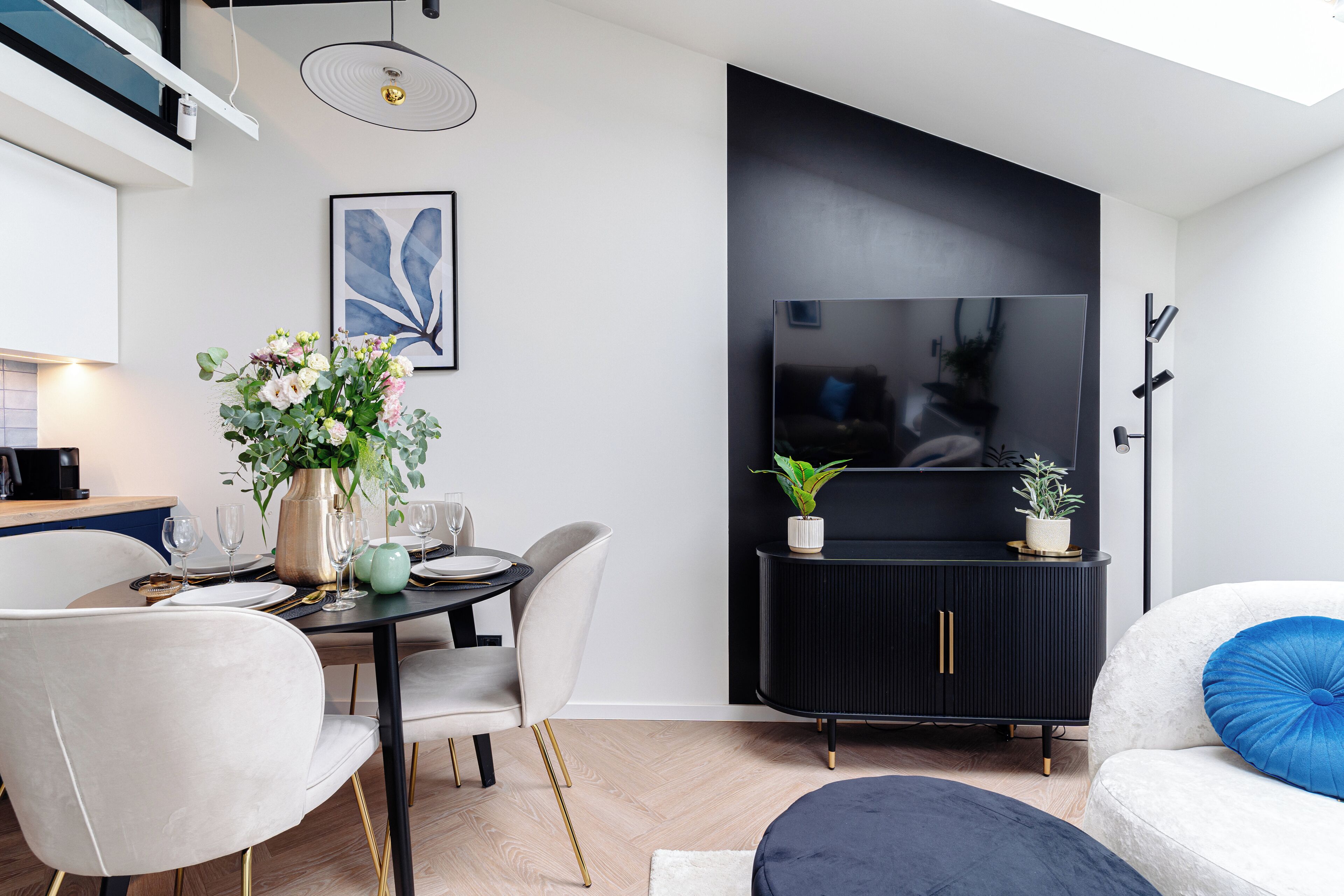 A modern living room with a dining area, a black entertainment unit, and a large flat-screen TV.