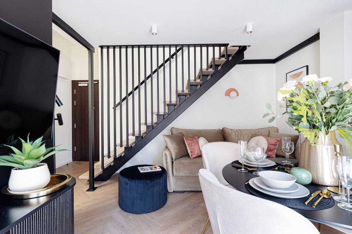Una sala moderna con una escalera, un sofá, un comedor y una planta en maceta.