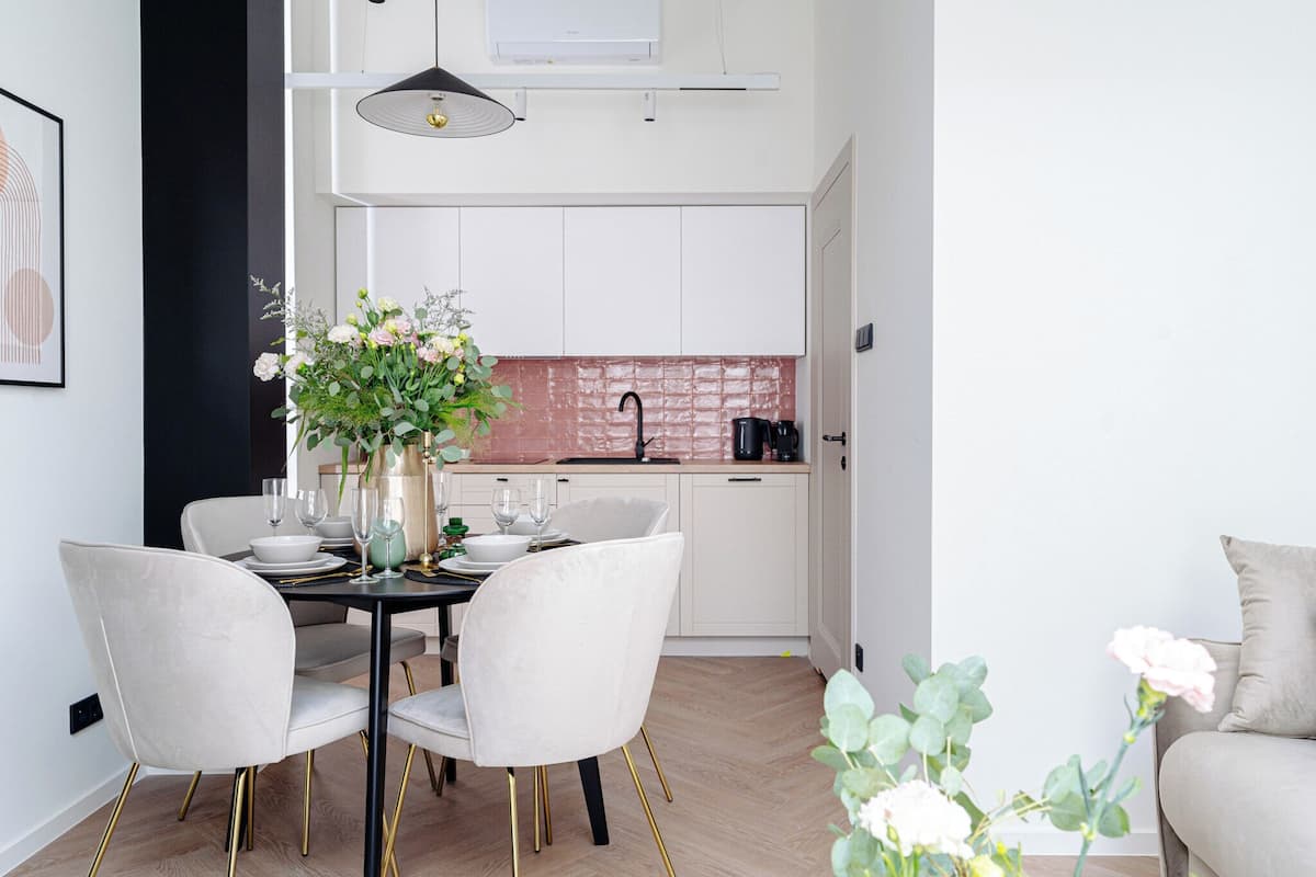 Una cocina moderna con gabinetes blancos, salpicadero rosa y un comedor con mesa puesta para cuatro.