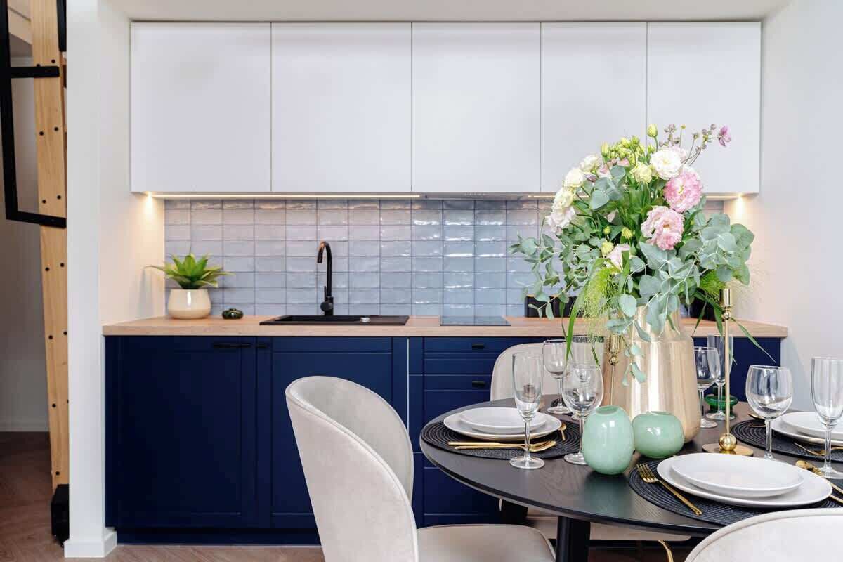 A modern kitchen with dark blue cabinets, a white backsplash, and a dining area with a round table set for four.