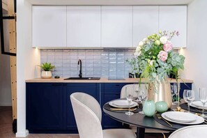 Een moderne keuken met donkerblauwe kastjes, een witte achterwand en een eethoek met een ronde tafel gedekt voor vier personen.