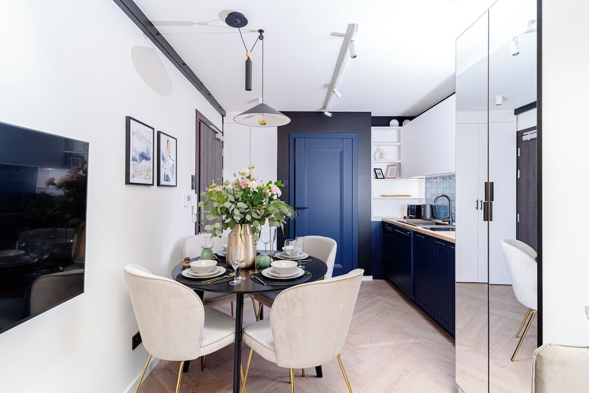 Un comedor moderno con una mesa redonda, cuatro sillas, un jarrón con flores y una cocina al fondo.