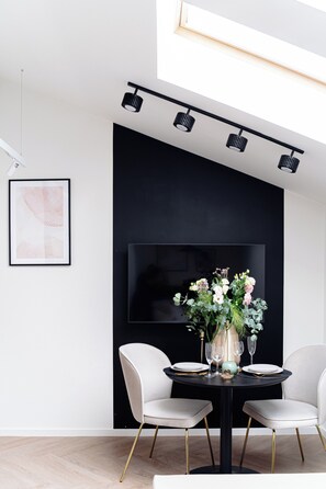 Een moderne eetruimte met een zwarte tafel, witte stoelen en een grote flatscreen televisie aan de muur.
