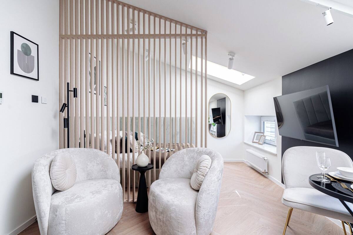 Una sala moderna con sofá, dos sillones, una mesa de comedor y un televisor, junto a un separador con listones verticales.
