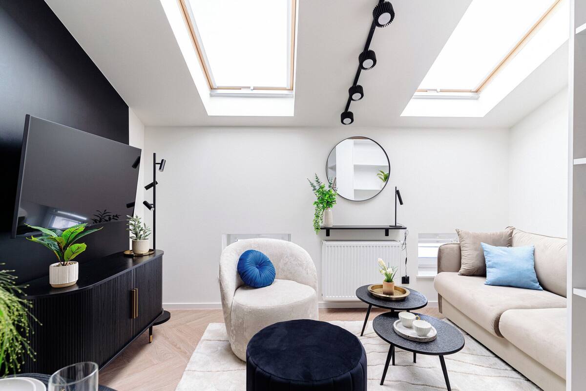 Una sala de estar moderna con un mueble de entretenimiento negro, un sofá blanco, un espejo redondo y un techo con tragaluces.