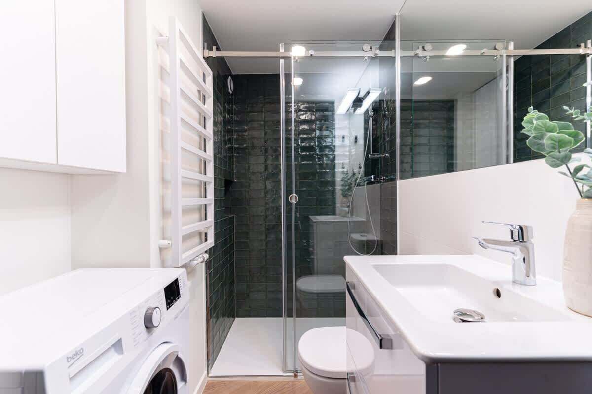 A modern bathroom with a glass shower enclosure, a washing machine, and a white sink.