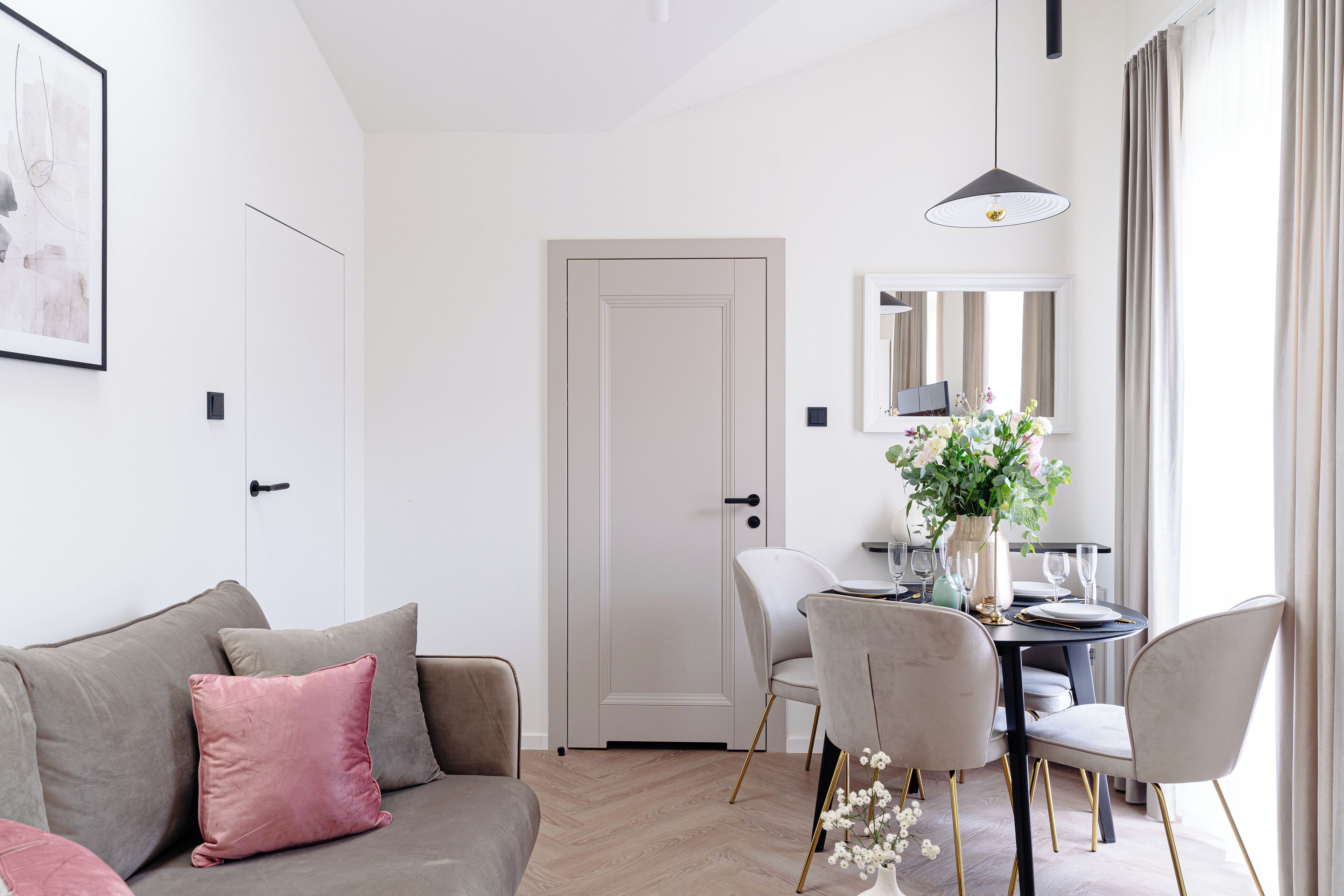 A modern living room with a sofa, a dining table with chairs, a door, and a hanging pendant light.