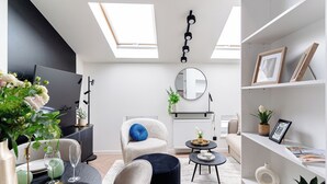A modern living room with a sofa, ottoman, and a dining table set with plates and glasses. There is a TV, a mirror, and a bookshelf with decorative items. - Miodova20 by StayLab (Kraków)