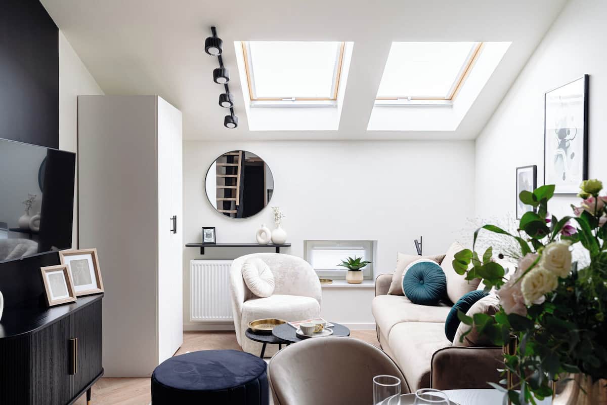 Una sala moderna con sofá, sillón y mesa de comedor. Hay tragaluces, un radiador y un televisor sobre un mueble.