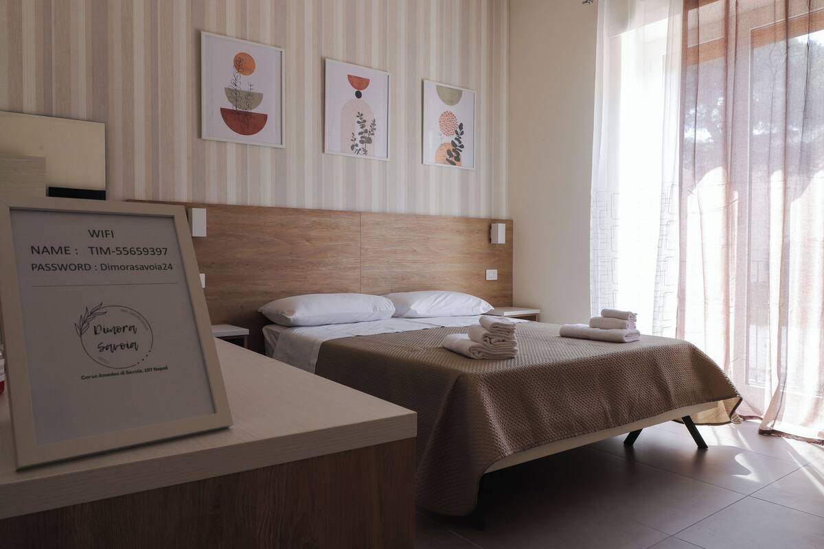 Habitación de hotel con cama, mesita de noche, cartel enmarcado con detalles de WiFi y una obra de arte en la pared.
