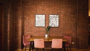 A dining area with a brick wall, a wooden table, and pink chairs. - Brick & Balcony Greeley Retreat (Greeley)