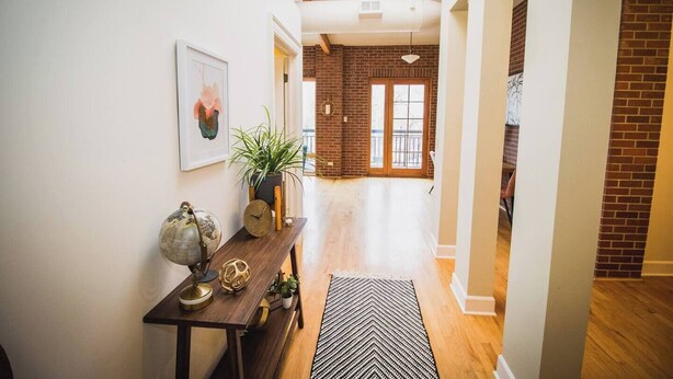 A hallway with a wooden bench, a globe, a clock, and a plant. There is a black and white rug on the floor. - Brick & Balcony Greeley Retreat (Greeley)