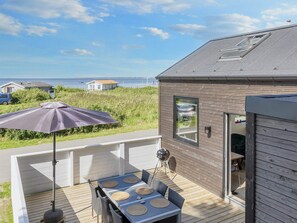 Una terraza con mesa y sillas, una parrilla y vista al mar.