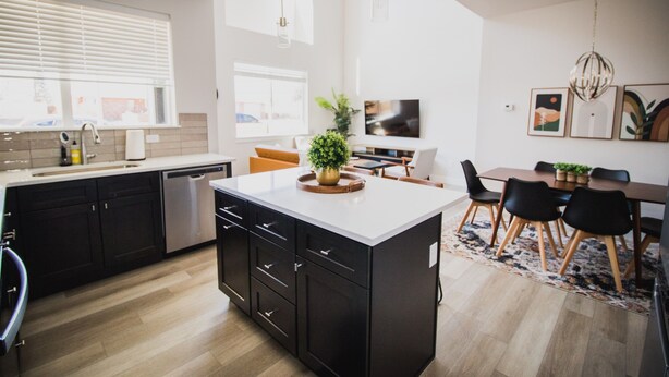Una cocina moderna con una isla central, armarios negros y un comedor con una mesa y sillas de madera.