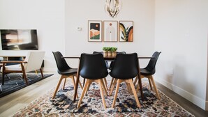 Un área de comedor con una mesa de madera, sillas negras y un tapete estampado. Hay tres obras de arte enmarcadas en la pared sobre la mesa.