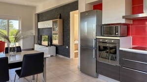 A modern kitchen with a stainless steel refrigerator, microwave, and oven. There is a dining area with a white table and black chairs. - Villa Adam (Chania)