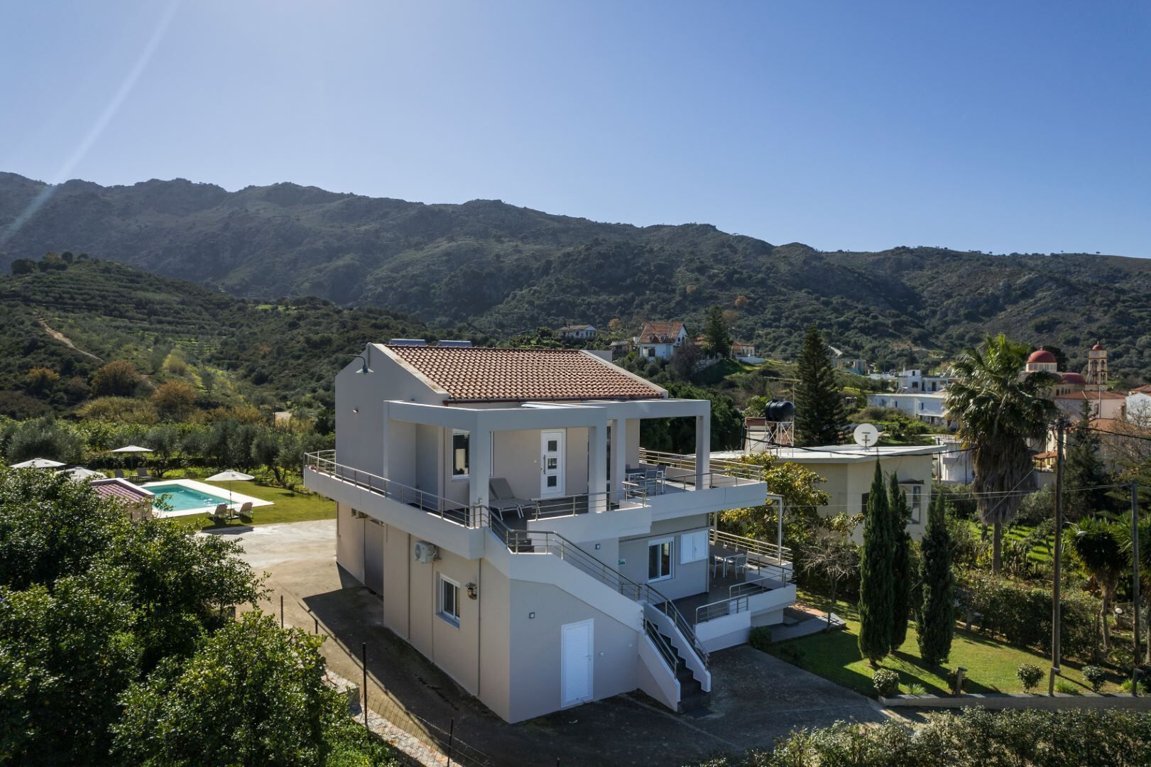 A modern two-story house with a balcony, a swimming pool, and a view of the surrounding hills.