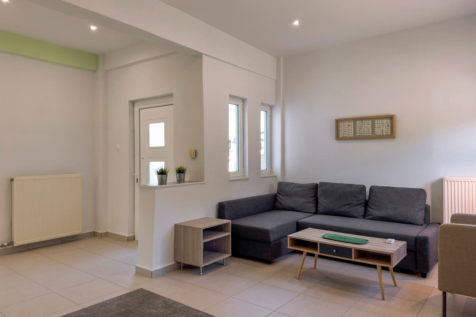 Uma sala de estar moderna com um sofá seccional cinzento, uma mesa de centro de madeira e um radiador.