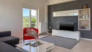 A modern living room with a flat-screen TV, a red chair, a white sofa, and a bookshelf. - Villa Adam (Chania)