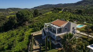 A modern two-story house with a swimming pool, surrounded by lush greenery and hills. - Villa Adam (Chania)