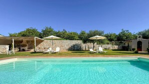 A clear swimming pool with lounge chairs and umbrellas, surrounded by a stone wall and greenery. - Villa Adam (Chania)