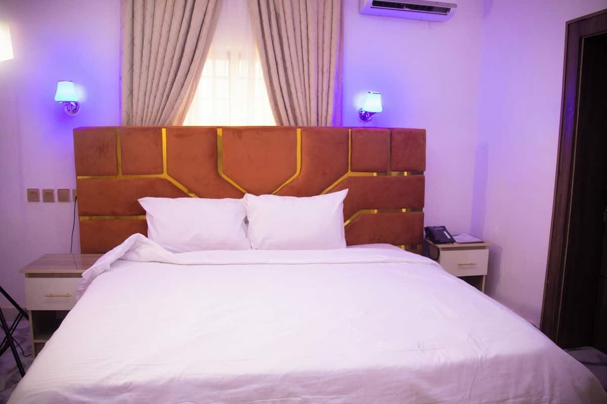 A hotel room with a large bed, two bedside tables, a nightstand, a lamp, and a window with curtains.