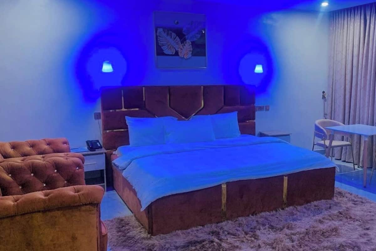 A bedroom with a large bed, two armchairs, a small table, and a window with curtains.