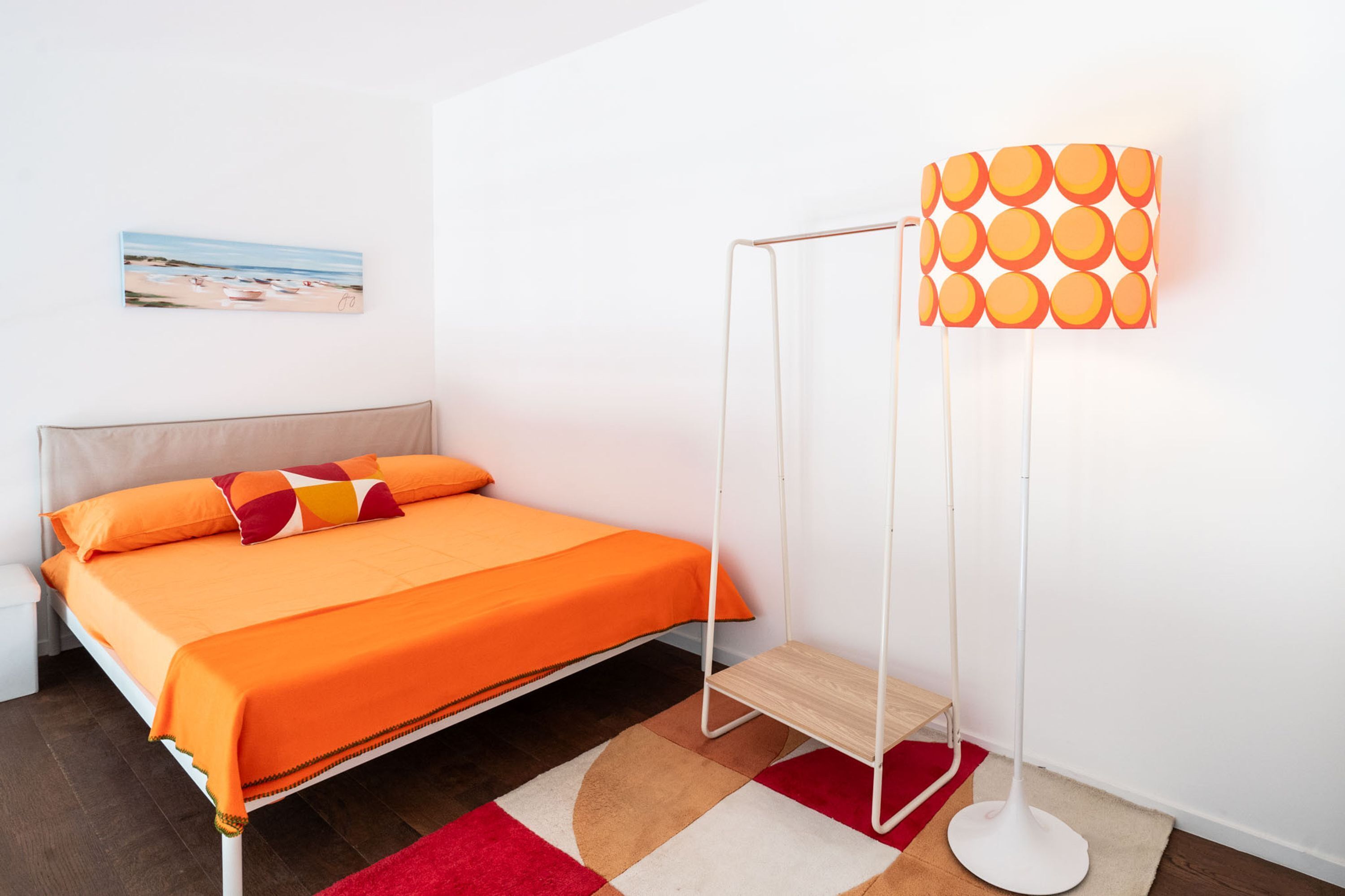 Une chambre à coucher avec un lit, une lampe de sol, un tableau et un tapis rouge.
