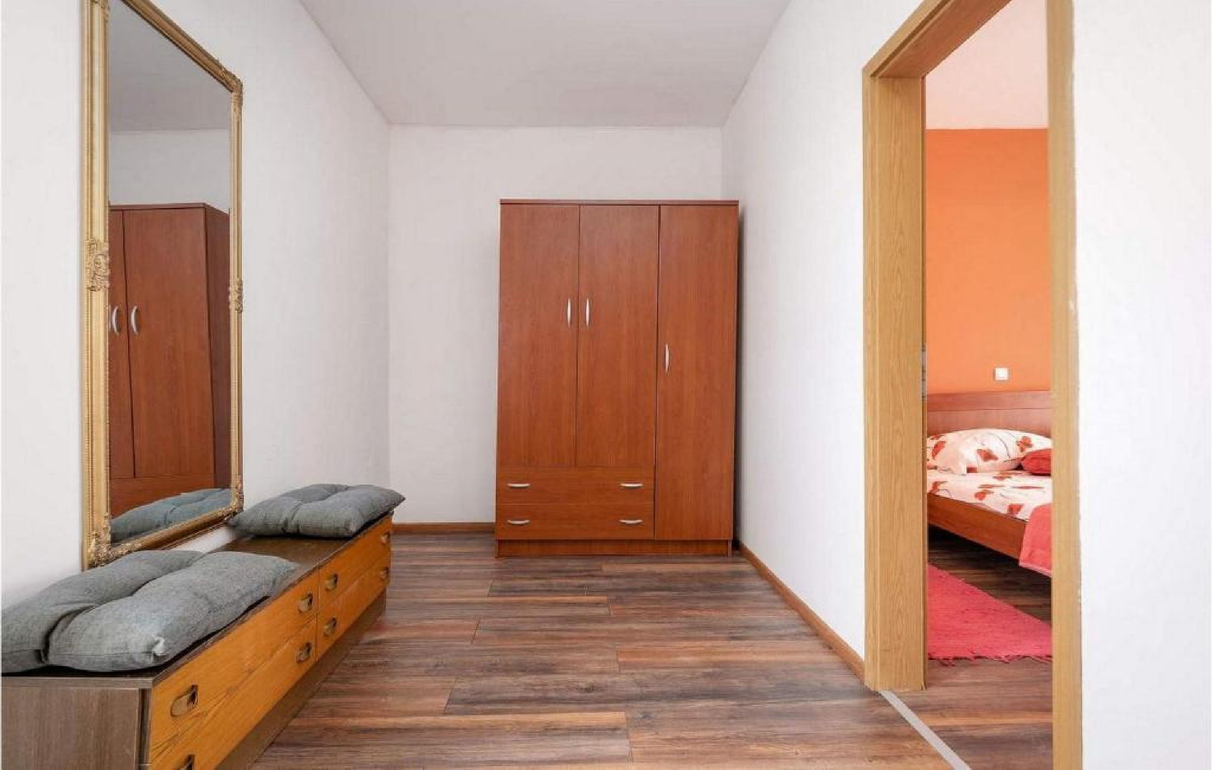 A bedroom with a wooden wardrobe, a bed, a mirror, and a dresser with drawers.