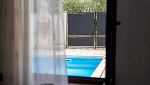 Vista attraverso una finestra su un'area piscina con recinzione e un edificio sullo sfondo.