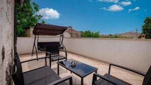 Una terrazza esterna con un'area salotto riparata, un tavolo e vista sugli edifici e sul cielo circostanti.