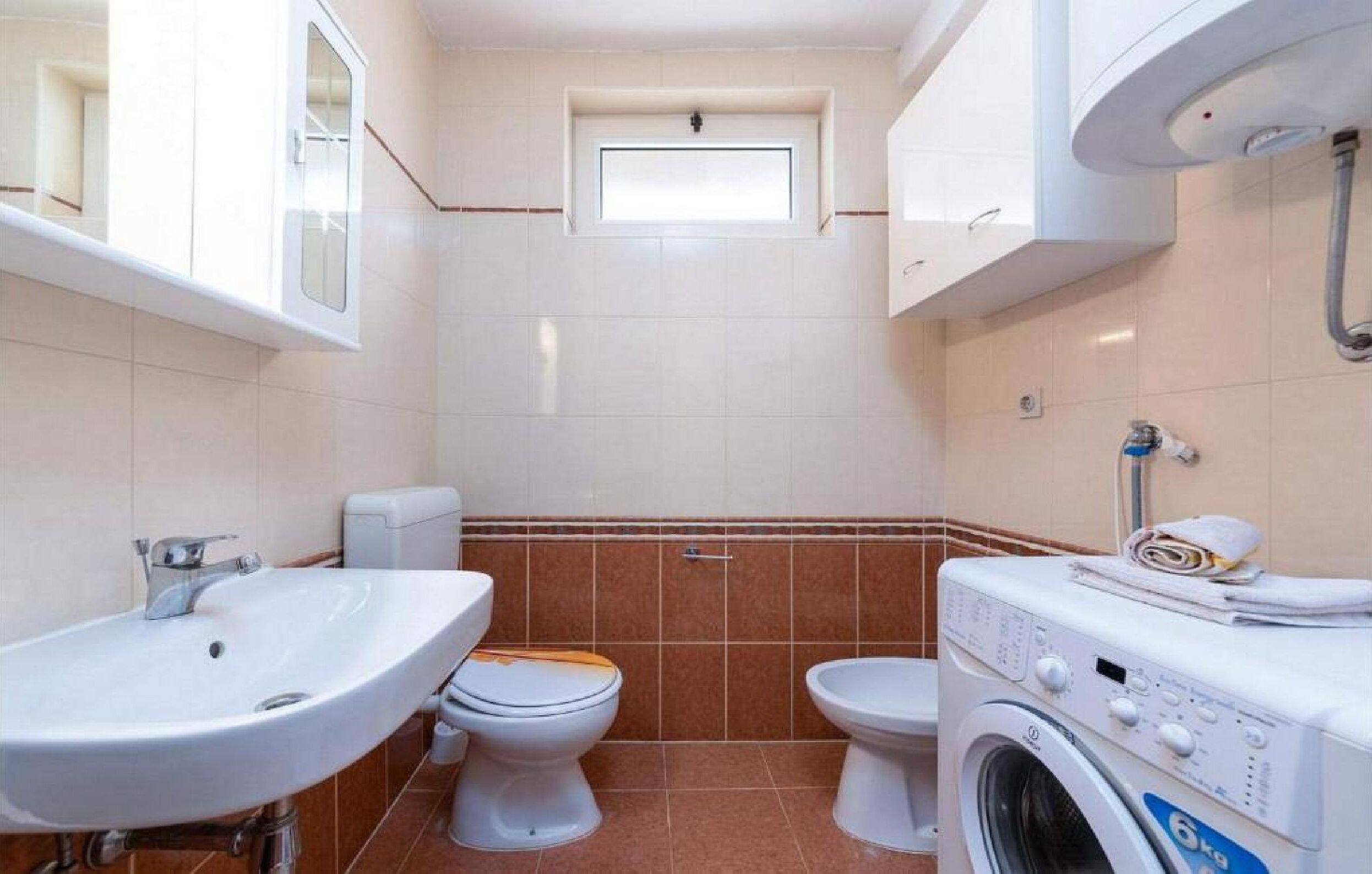 Une petite salle de bain comprenant un lavabo, deux toilettes, une fenêtre et un lave-linge.